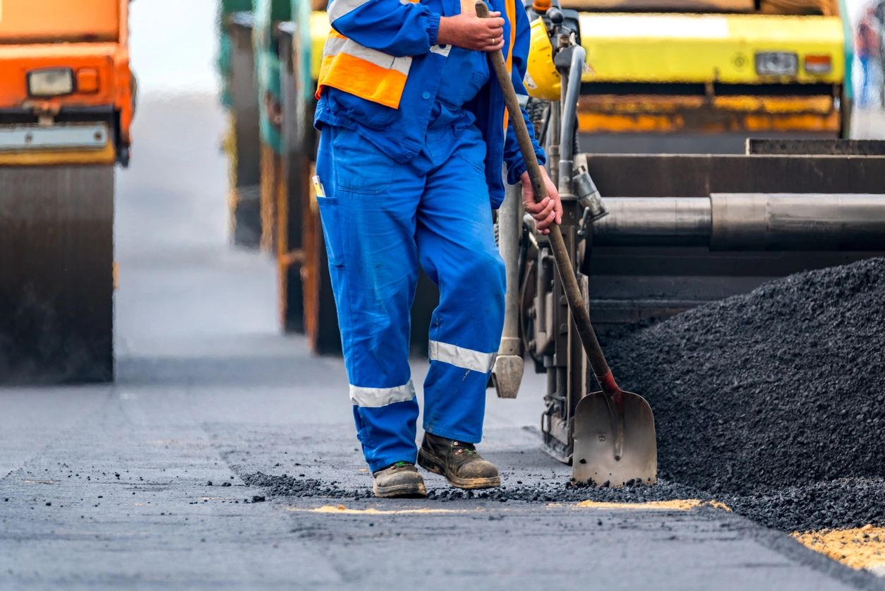 A man in blue work clothes standing next to a road.